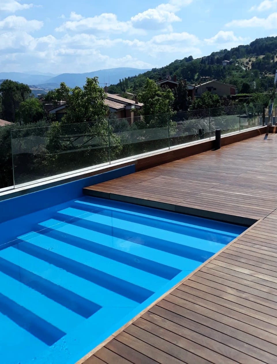 Piscina a sfioro con decking in legno e vista sulle colline